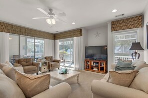 A spacious living room with a ceiling fan, large windows, a flat-screen TV, and a comfortable seating area. - Villa 18 at Hidden Dunes (Miramar Beach)