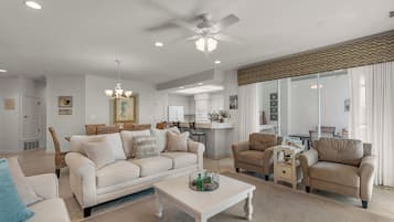 A spacious living room with a white sofa, beige armchairs, a coffee table, and a ceiling fan.