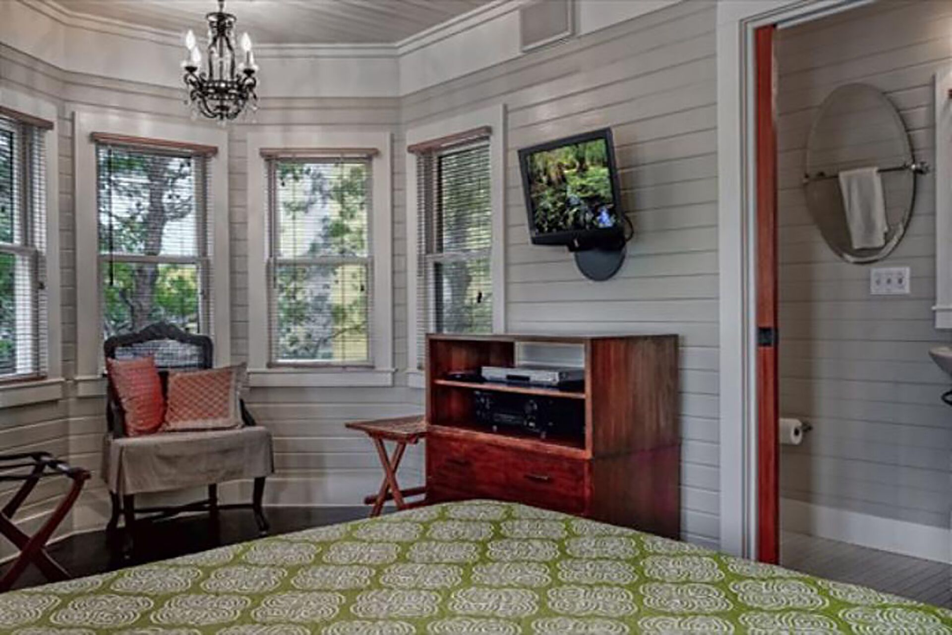 A bedroom with a bed, a TV mounted on the wall, a small table, and a chair.