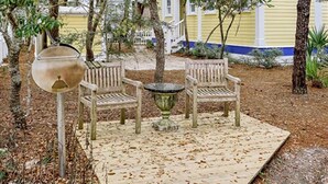 An outdoor seating area with a table and two chairs, surrounded by trees and a wooden deck. - Turkish Delight in Seaside (Santa Rosa Beach)