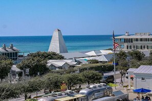A coastal town with a prominent lighthouse, a flagpole with an American flag, and a variety of buildings including a large house with a white facade.
