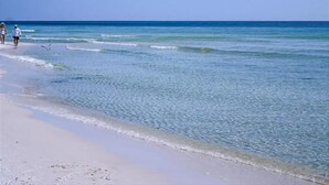 A beach with clear water and a few people walking along the shore. - Turkish Delight in Seaside (Santa Rosa Beach)