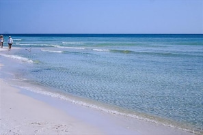 A beach with clear water and a few people walking along the shore.