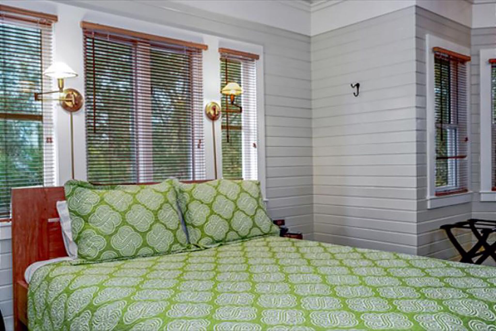 A bedroom with a bed, two windows with blinds, and a nightstand.