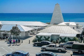 A coastal building with a prominent pyramid-shaped structure, adjacent to a parking area with several cars.