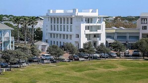 A white building with multiple floors and a flat roof, surrounded by parked cars and greenery. - Turkish Delight in Seaside (Santa Rosa Beach)