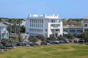 A white building with multiple floors and a flat roof, surrounded by parked cars and greenery. - Turkish Delight in Seaside (Santa Rosa Beach)