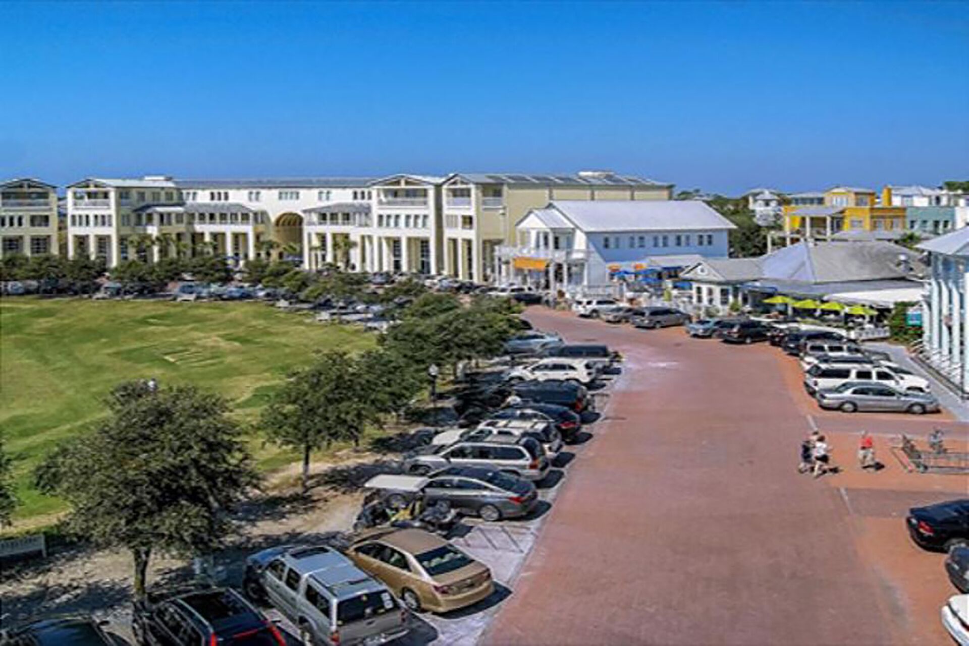 Un parking rempli de voitures, un bâtiment à la façade de couleur claire et un ciel bleu dégagé.