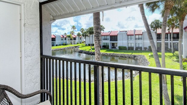 A view from a balcony with a pool, palm trees, and a row of buildings with red roofs. - Runaway Bay Resort by BBG (Bradenton Beach)