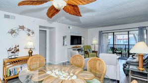 Ein Wohnzimmer mit einem Esstisch aus Glas, umgeben von Korbstühlen, einem Sofa und einem Fernseher.