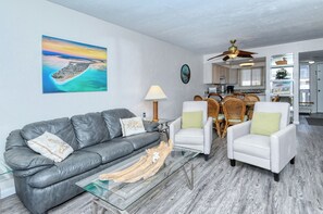 A living room with a gray leather sofa, white armchairs, a glass coffee table, and a wooden floor. - Runaway Bay Resort by BBG (Bradenton Beach)