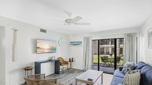 Una sala moderna con sofá, sillas, una mesa de centro, televisor y un balcón con mobiliario exterior.
