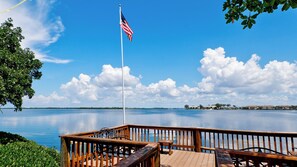 A wooden deck with a flagpole and a flag, overlooking a calm body of water with a distant shoreline. - Runaway Bay Resort by BBG (Bradenton Beach)
