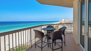 Un balcon avec vue sur la plage et l’océan, agrémenté de fauteuils en osier et d’une petite table.