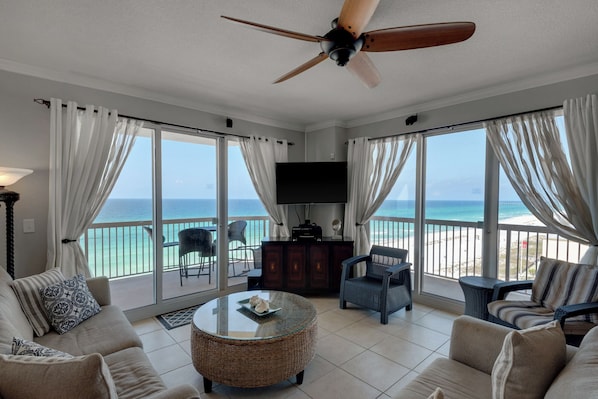 A spacious living room with a large TV, comfortable seating, and a view of the beach.