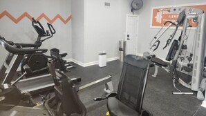 Ein Fitnessraum mit einem Ergometer, einer Gewichtshalterung und einem an der Wand befestigten Trainingsgerät.