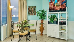 Un salon avec un téléviseur, une table à manger avec des chaises, une plante en pot et une vue sur l’océan.
