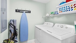 A laundry room with a washing machine, a drying rack, and a shelf with laundry baskets.