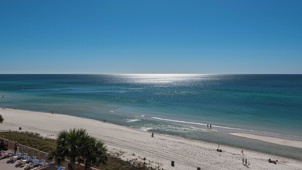 A beach with clear blue water, a sandy shore, and a few people walking.