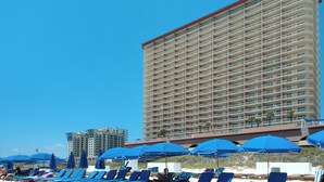 A beachfront hotel with multiple balconies, sun loungers, and blue umbrellas.