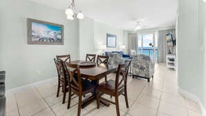 A dining area with a wooden table and chairs, a ceiling fan, and a view of the living room with a sofa and chairs.