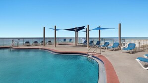 A pool area with lounge chairs and umbrellas, a clear view of the ocean, and a lifeguard stand.