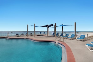 A pool area with lounge chairs and umbrellas, a clear view of the ocean, and a lifeguard stand. - Sunrise Resort by BBG (Panama City Beach)