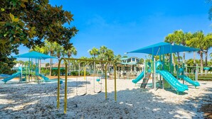 Un parque infantil con columpios y toboganes, rodeado de palmeras y cubierto por toldos azules.