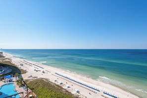 A beach resort with a swimming pool, beach umbrellas, and a pier in the background.