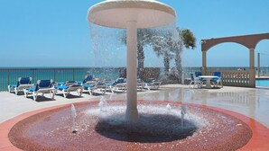 A water fountain surrounded by lounge chairs and a poolside area with a clear view of the ocean.