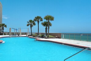 A swimming pool with a clear blue water, surrounded by palm trees and a view of the ocean.