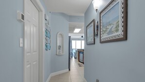 A hallway with light blue walls, a white door, and a kitchen visible in the distance.