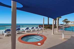 Zona de piscina con sillones de descanso y un jacuzzi, con vista al océano.