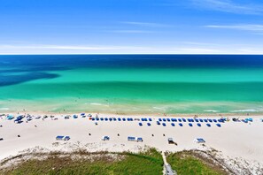 Ein Strand mit Reihen blauer Sonnenschirme und Liegestühle, ein klarer, blauer Himmel und ruhiges Meer.