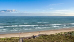 Une plage avec une promenade en bois menant au rivage, un ciel dégagé et une mer calme.