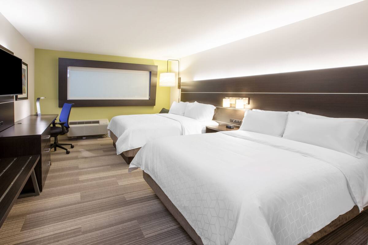 A hotel room with two beds, a desk, a chair, a TV, and a large window.