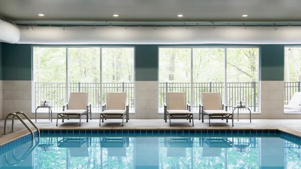 A swimming pool with four lounge chairs and a view of trees through large windows. - Holiday Inn Express & Suites Harrisburg S - Mechanicsburg by IHG (Mechanicsburg)