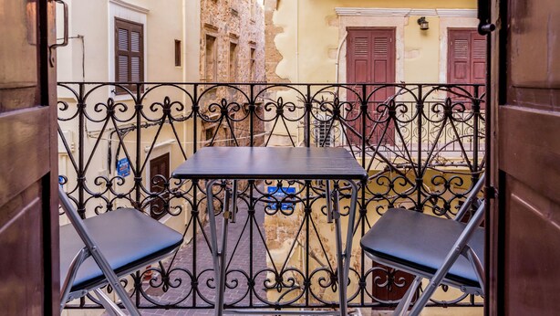 A narrow alleyway with a small table and two chairs, enclosed by ornate metal railings. - Alegria (Chania)
