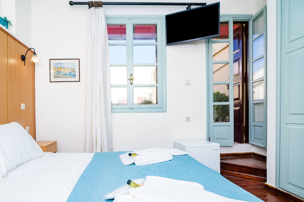 A hotel room with a bed, a TV mounted on the wall, a window with curtains, and a door leading to a staircase.
