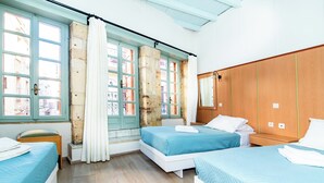 A room with two beds, a wooden wardrobe, a window with curtains, and a view of buildings outside. - Alegria (Chania)