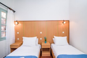 A double room with two beds, wooden headboard, bedside tables, a small potted plant, and a window with curtains. - Alegria (Chania)
