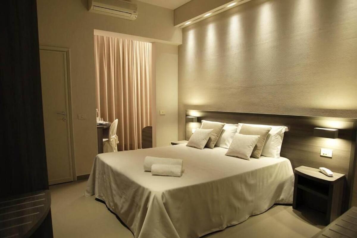 A modern hotel room with a large bed, a bedside table with a phone, and a window with curtains.