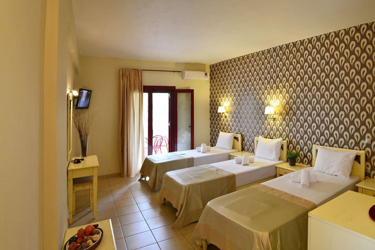 A hotel room with two beds, a TV, a desk, and a window with curtains.