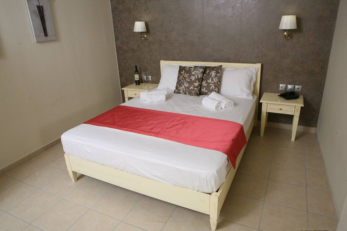 A double bed with a red and white bedspread, two bedside tables with lamps, and a wall-mounted light fixture.