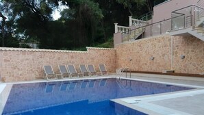 Una piscina con muro de piedra, barandilla de vidrio y escalera que sube a un nivel superior.