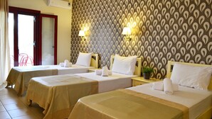 Habitación de hotel con tres camas individuales, cada una con una almohada blanca y una toalla. Hay dos lámparas de pared y una pequeña planta en maceta sobre la mesita de noche.