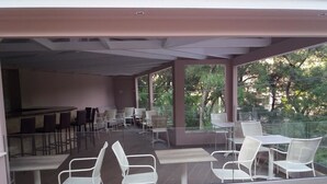 Un área de comedor exterior moderna con paredes de vidrio, sillas y mesas blancas.