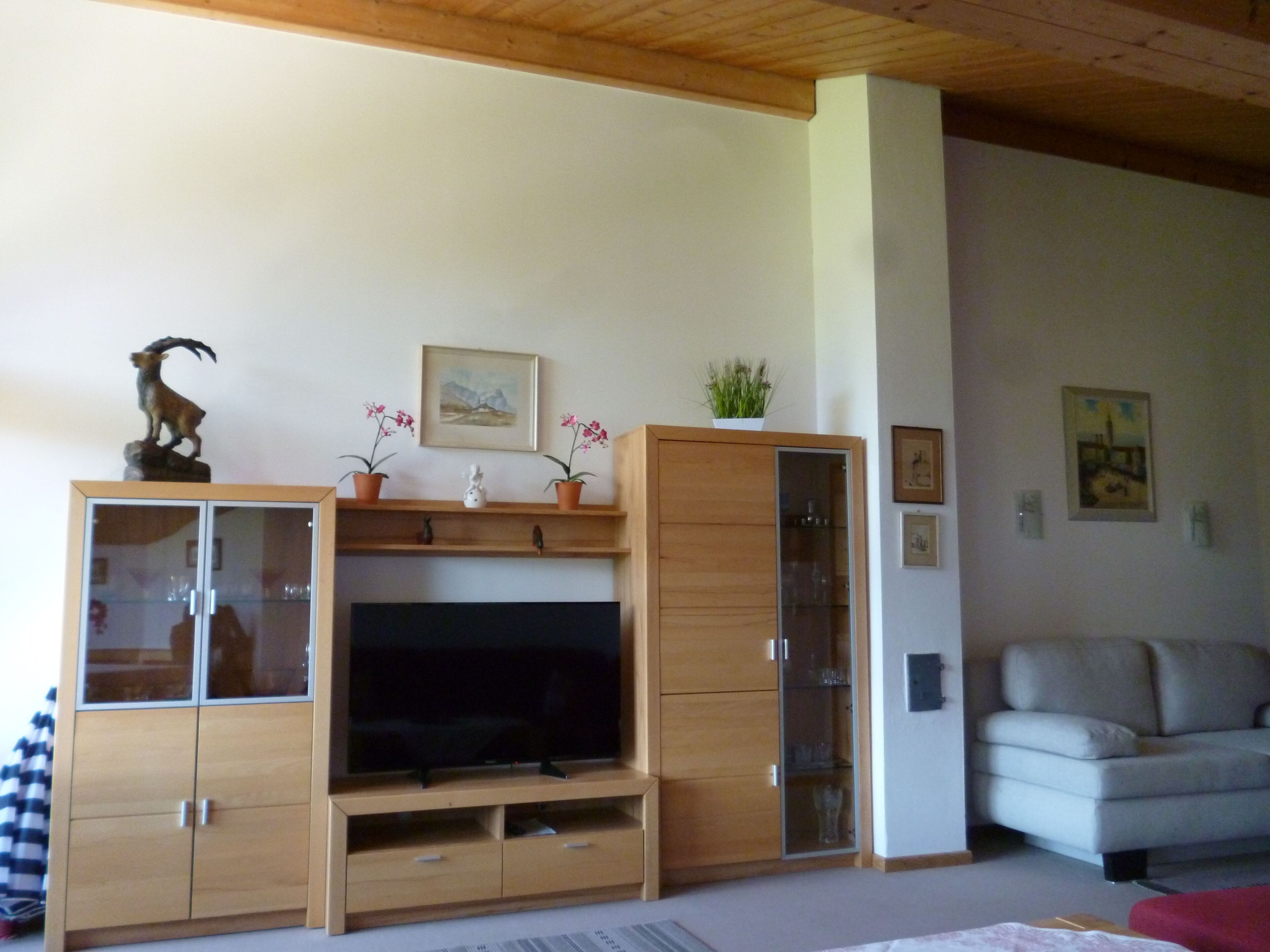 Ein Wohnzimmer mit einer Holztrennwandschranke, einem Flachbildfernseher, einer Couch und einem roten Hocker.