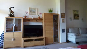Ein Wohnzimmer mit einer Holztrennwandschranke, einem Flachbildfernseher, einer Couch und einem roten Hocker.