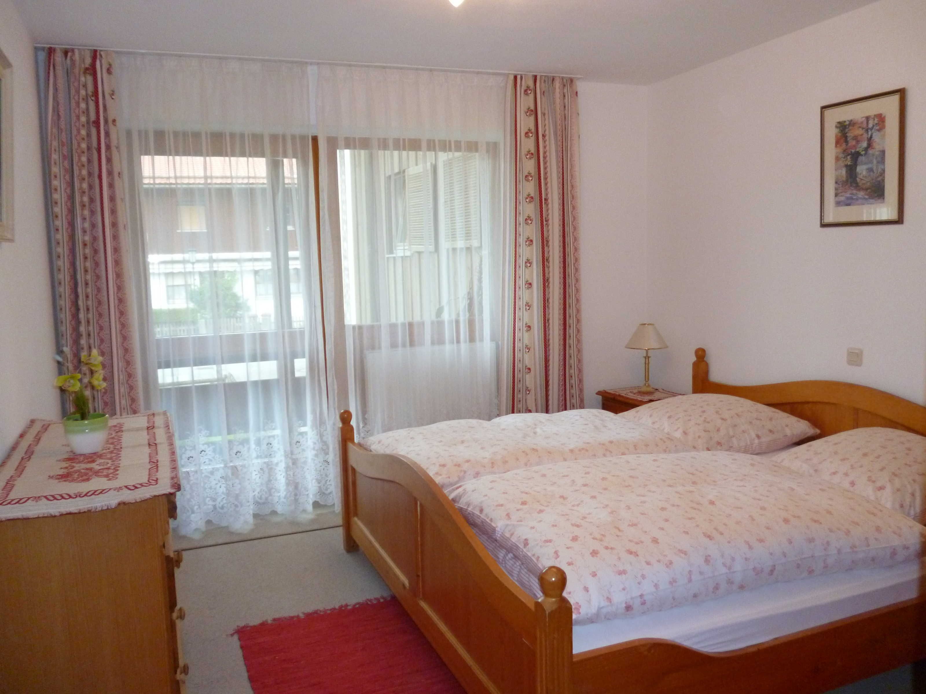Un dormitorio con una cama doble, una mesita de noche con lámpara, un aparador y una ventana con cortinas.